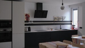 Une cuisine moderne dotée d’un four encastré, d’une hotte noire, d’un évier et d’un coin repas avec une table et des chaises.