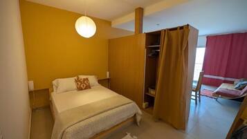 Un dormitorio con cama, armario, lámpara colgante y ventana con cortinas.