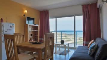 Una habitación con una mesa de comedor, sillas, un sofá, un televisor, una estantería y vistas al mar.
