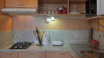 Una cocina con estufa a gas, cafetera y microondas. Hay armarios y un lavamanos.