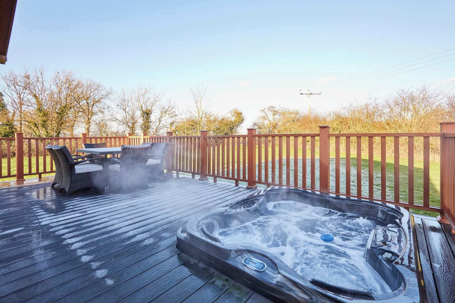 Ein Whirlpool auf einer Holzterrasse mit Holzzaun, Grill und Tisch mit Stühlen.