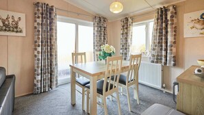 A room with a wooden dining table, four chairs, a vase with flowers, a radiator, and patterned curtains. - Host & Stay | ORC02 Hidden Gem Lodge (Amotherby)