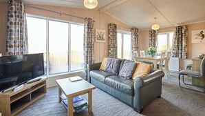 A living room with a sofa, coffee table, TV, and a dining area with chairs and a table. - Host & Stay | ORC02 Hidden Gem Lodge (Amotherby)