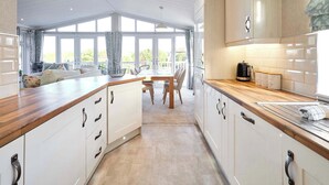 A modern kitchen with white cabinetry, a wooden countertop, and a dining area with a view. - Host & Stay | GRE06 Deneb Lodge (Amotherby)