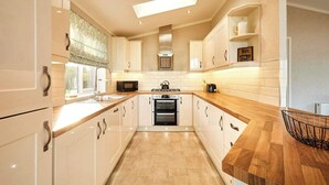 A modern kitchen with white cabinetry, a wooden countertop, a built-in oven, and a skylight. - Host & Stay | GRE06 Deneb Lodge (Amotherby)