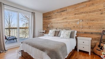 Une chambre avec un mur en bois, un lit avec des oreillers, une table de chevet, une guitare et un balcon avec des chaises.