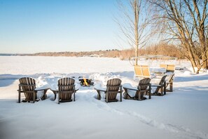 Een terras buiten bedekt met sneeuw, met Adirondack-stoelen en een vuurkorf.