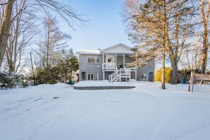 Une maison à deux étages avec un porche à l’avant et une allée recouverte de neige.