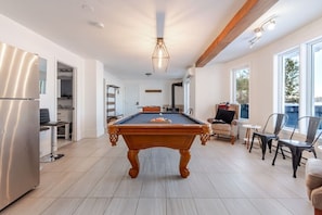 Une pièce spacieuse équipée d’une table de billard, d’un coin salon avec des fauteuils et d’un réfrigérateur.