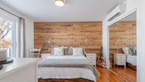 Une chambre avec un mur en bois, un lit avec une literie blanche, une table de chevet, une guitare et un miroir.