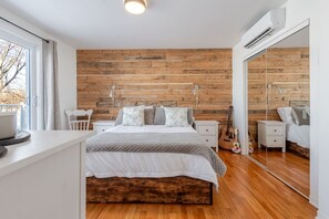 Une chambre avec un mur en bois, un lit avec une literie blanche, une table de chevet, une guitare et un miroir.