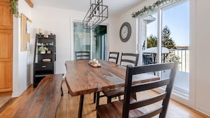 Un coin repas avec une table et des chaises en bois, une étagère noire et une vue sur l’extérieur grâce à une porte vitrée.