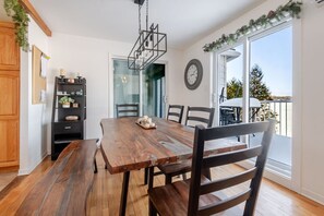 Un coin repas avec une table et des chaises en bois, une étagère noire et une vue sur l’extérieur grâce à une porte vitrée.