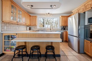 A kitchen with wooden cabinets, a stainless steel refrigerator, and a large island with stools.