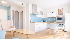Eine moderne Küche mit weißen Schränken, einer blauen Spritzschutzwand und einer Mikrowelle. Ein Essbereich mit Tisch und Stühlen ist ebenfalls vorhanden.
