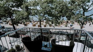 A balcony with wicker chairs and a table, overlooking a street with parked bicycles and trees.