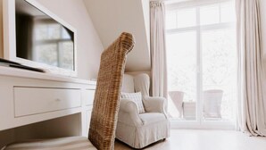 A modern room with a television, a wicker chair, a sofa, and a view through a large window.