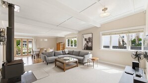 A spacious living room with a large gray sectional sofa, a wooden coffee table, a fireplace, and a dining area with a table and chairs. - 1920s Character Gem in Sandringham | Garden & Deck (Auckland Central)