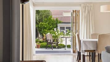A room with a dining table, chairs, a sofa, and a view of a garden and neighboring buildings.