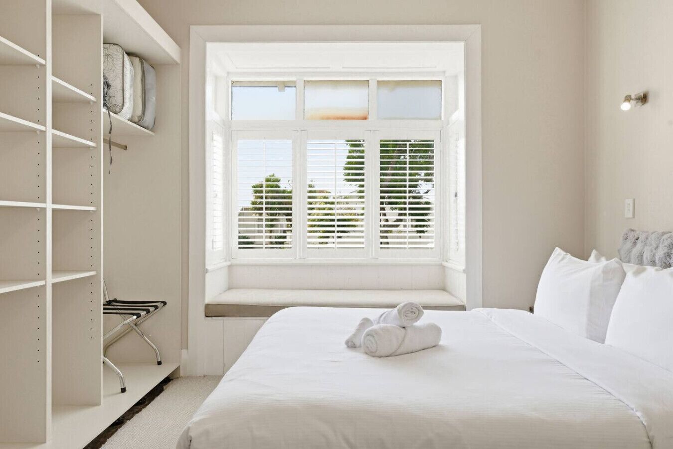 A bedroom with a bed, a window with blinds, a wardrobe, and a bench.