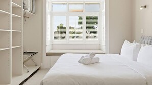 A bedroom with a bed, a window with blinds, a wardrobe, and a bench. - 1920s Character Gem in Sandringham | Garden & Deck (Auckland Central)