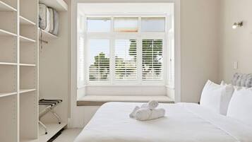 A bedroom with a bed, a window with blinds, a wardrobe, and a bench.