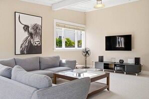 A living room with a grey sofa, a coffee table, a TV, and a speaker system. - 1920s Character Gem in Sandringham | Garden & Deck (Auckland Central)