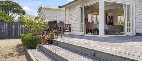 Una casa a due piani con un patio in legno, posti a sedere all'aperto e un cortile recintato.