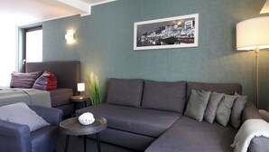 A modern living room with a grey sofa, a small round table, a lamp, and a framed black and white photo on the wall. - Appartement Nr. 05 (Rostock)