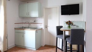 A small kitchen with a sink, cabinets, and a dining area with two chairs and a table. - Appartement Nr. 05 (Rostock)