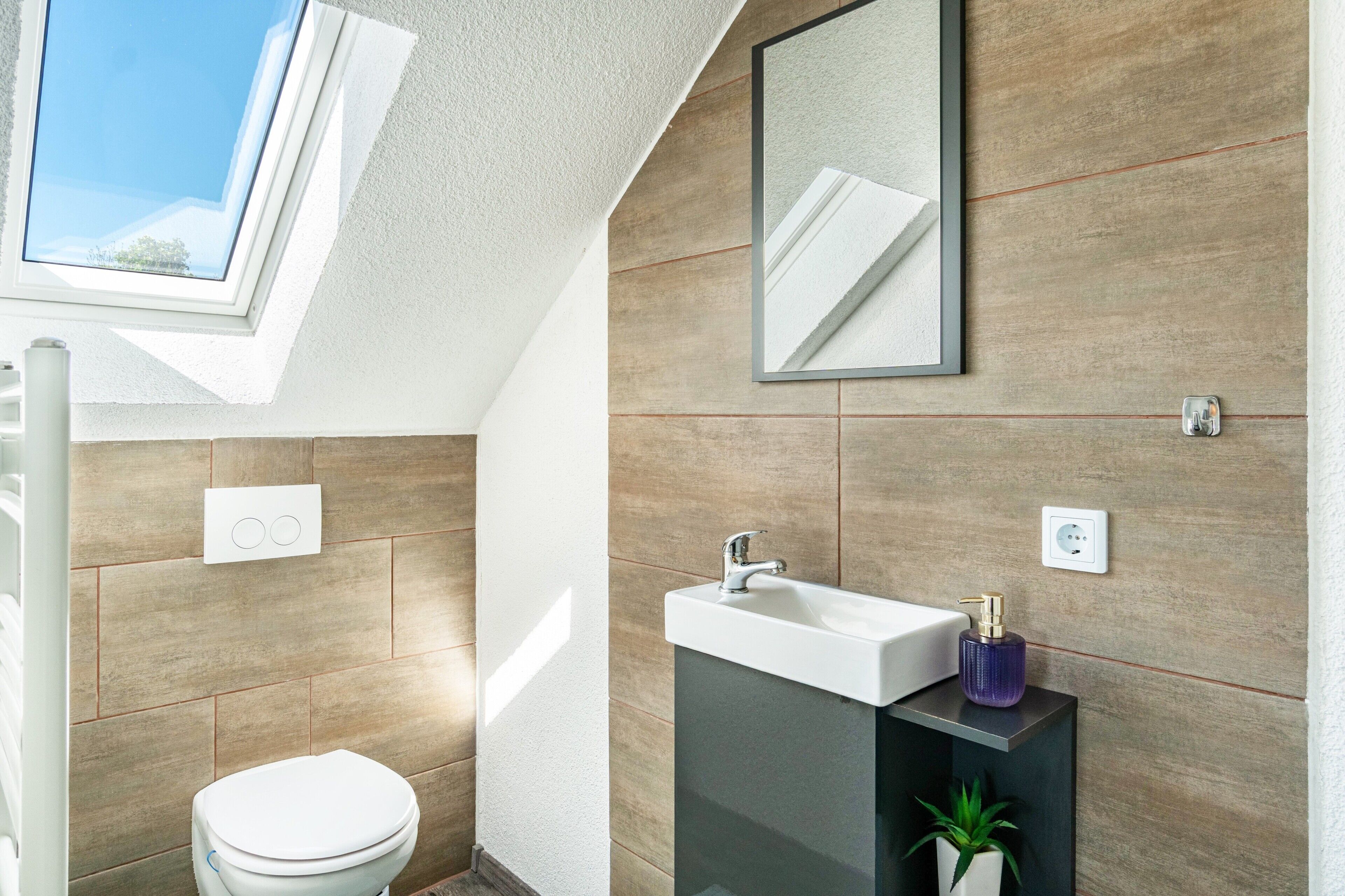 Une salle de bain moderne avec un puits de lumière, des toilettes, un lavabo et un miroir.