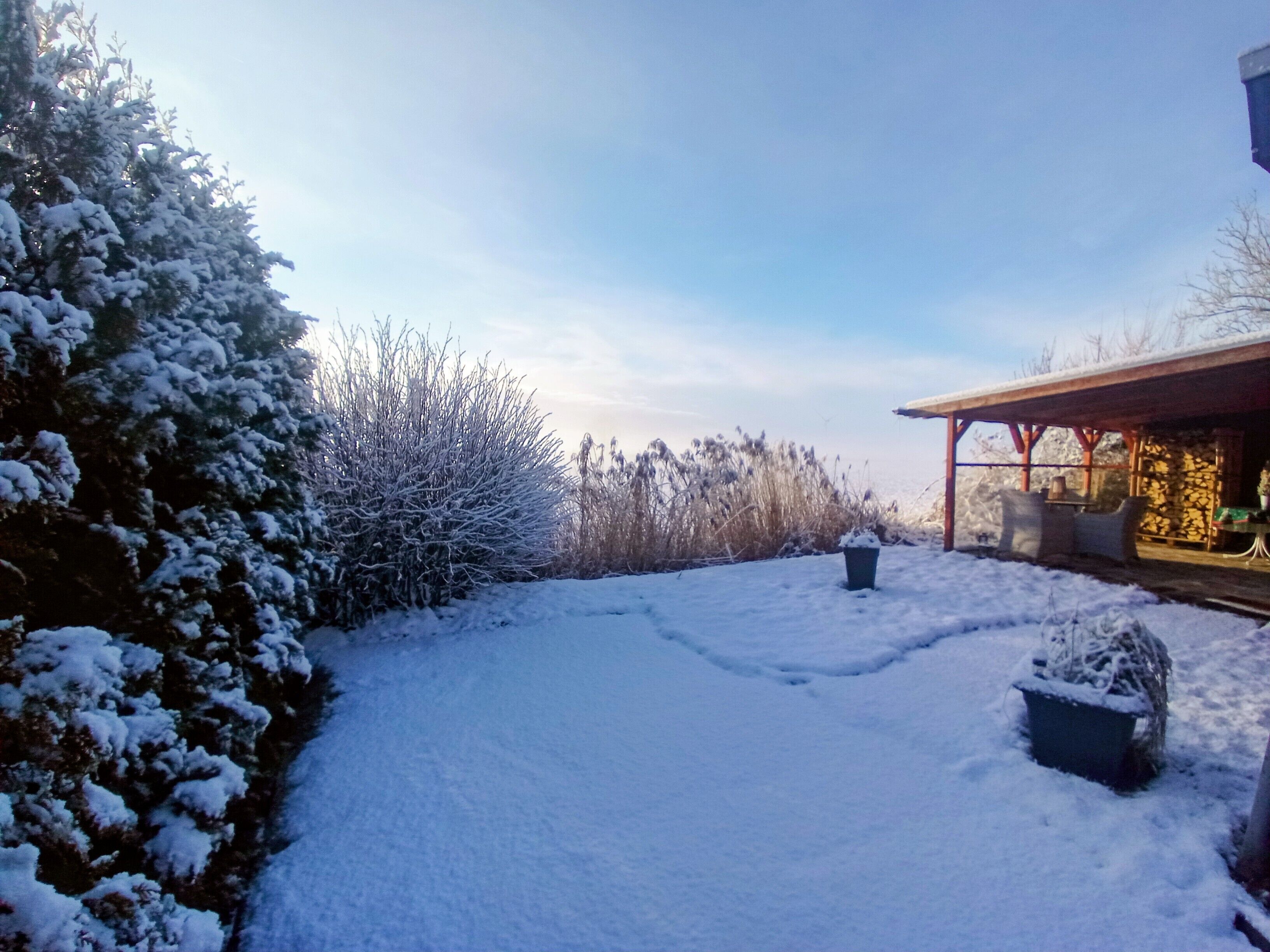 Ein mit Schnee bedeckter Garten mit einer Steinmauer und einer Holzhütte.