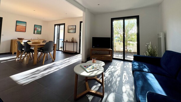 Una sala de estar moderna con sofá, mesa de centro, televisor y comedor con sillas y mesa.