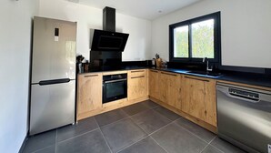 Una cocina moderna con refrigerador de acero inoxidable, horno empotrado, lavavajillas, armarios de madera y una ventana que proporciona luz natural.