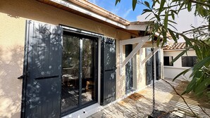 Una casa con puerta corredera de vidrio, un patio de piedra y un árbol en primer plano.