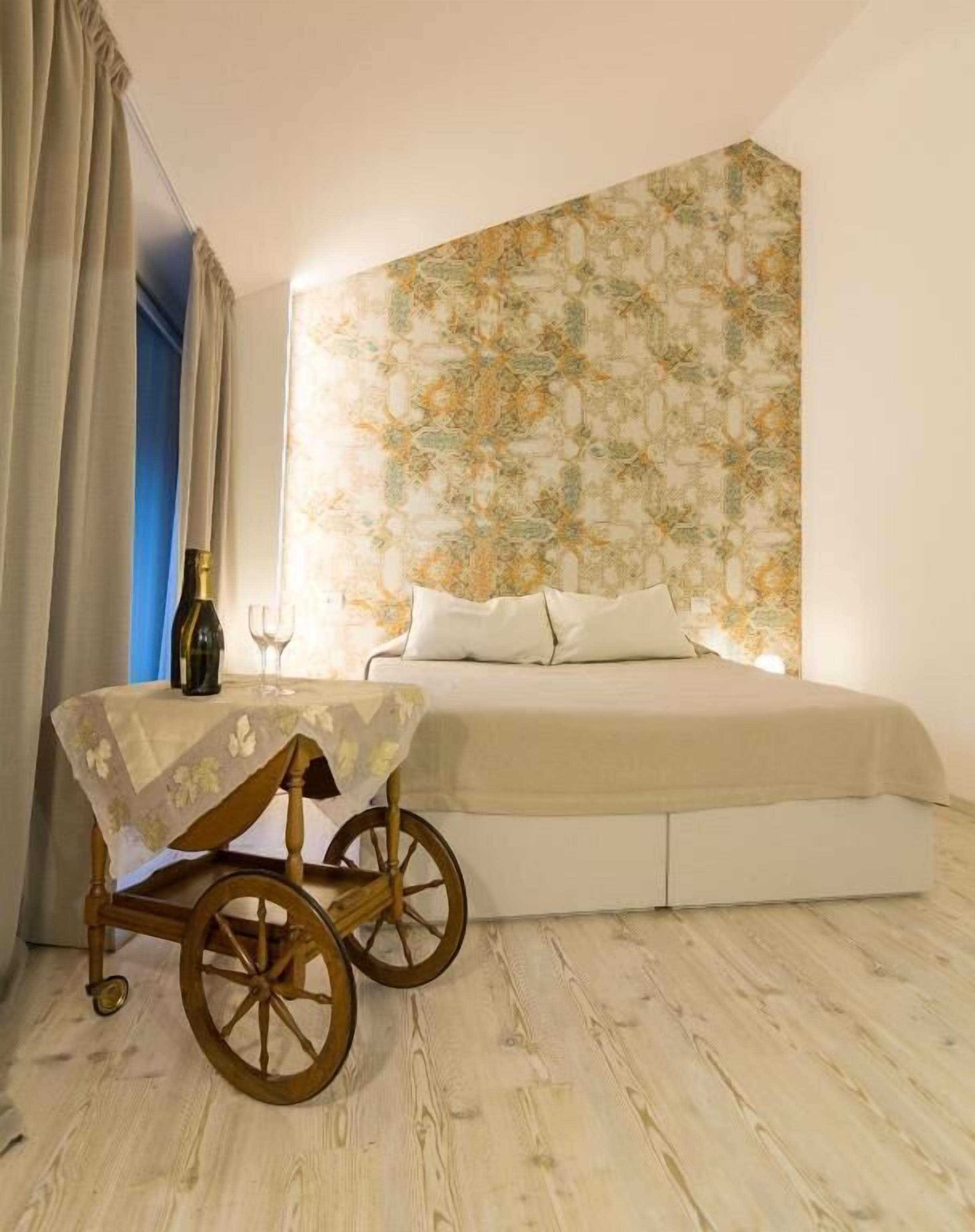 Een slaapkamer met een bed, een houten stoel, een tafel met een fles en een glas, en een behang met een patroon.