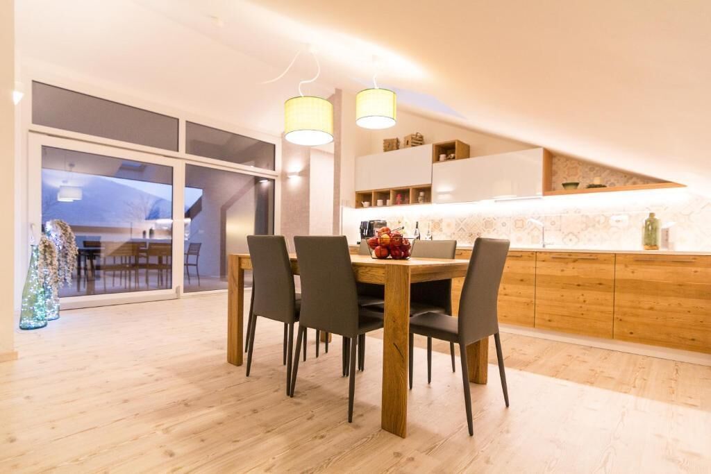 A modern dining area with a wooden table and chairs, a kitchen with wooden cabinets, and a large window.
