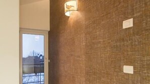 Un pasillo con suelo de madera, pared con textura y una puerta que da a un balcón.