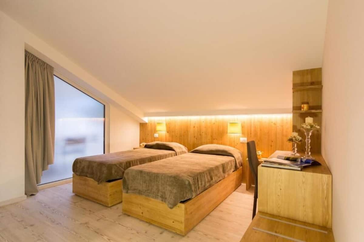 A bedroom with two beds, a desk, and a large window.