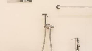 Een badkamer met toilet, bidet en wastafel, een handgreep en twee gouden vazen met bloemen.