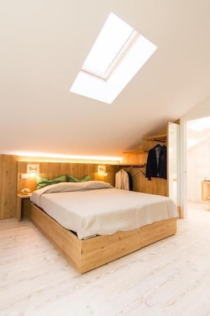 A bedroom with a skylight, wooden headboard, bedside lamps, and a bed with a white mattress.