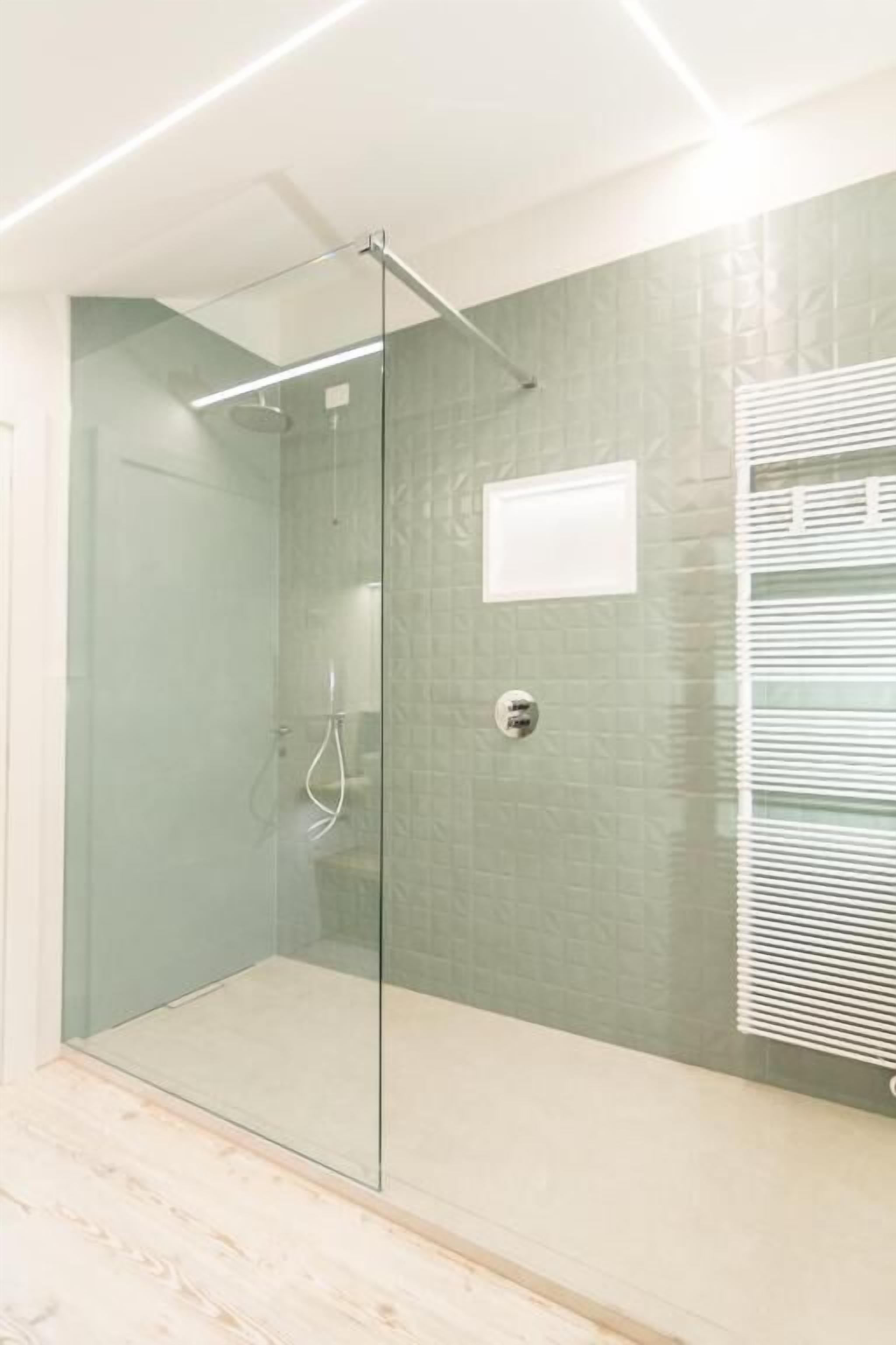 A modern bathroom with a glass shower enclosure, a tiled wall, and a white ceiling light.