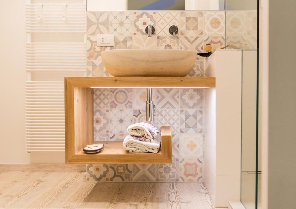Un baño con estante de madera con toallas, un lavamanos grande tipo cuenco y azulejos estampados.