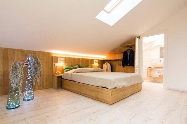 Une chambre avec un puits de lumière, des murs en bois, un lit, des tables de chevet et une armoire.