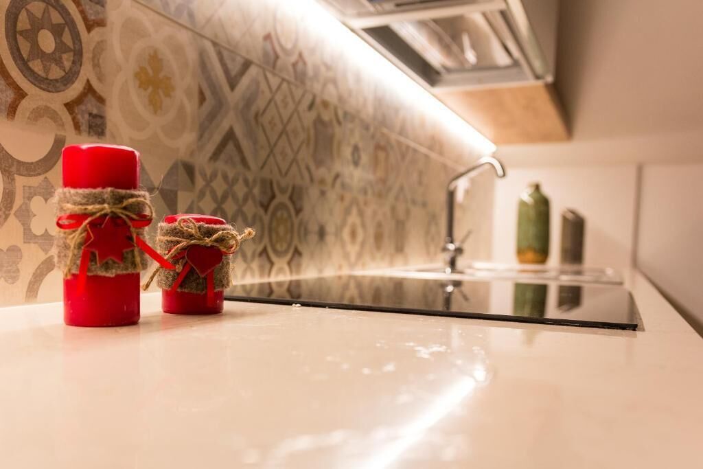 A kitchen with a modern stove, a patterned backsplash, and two red candle holders with twine and heart decorations.