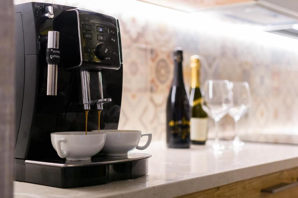 Eine Kaffeemaschine, die Kaffee in zwei Tassen füllt, eine Weinflasche und zwei Weingläser auf einer Küchenarbeitsplatte.