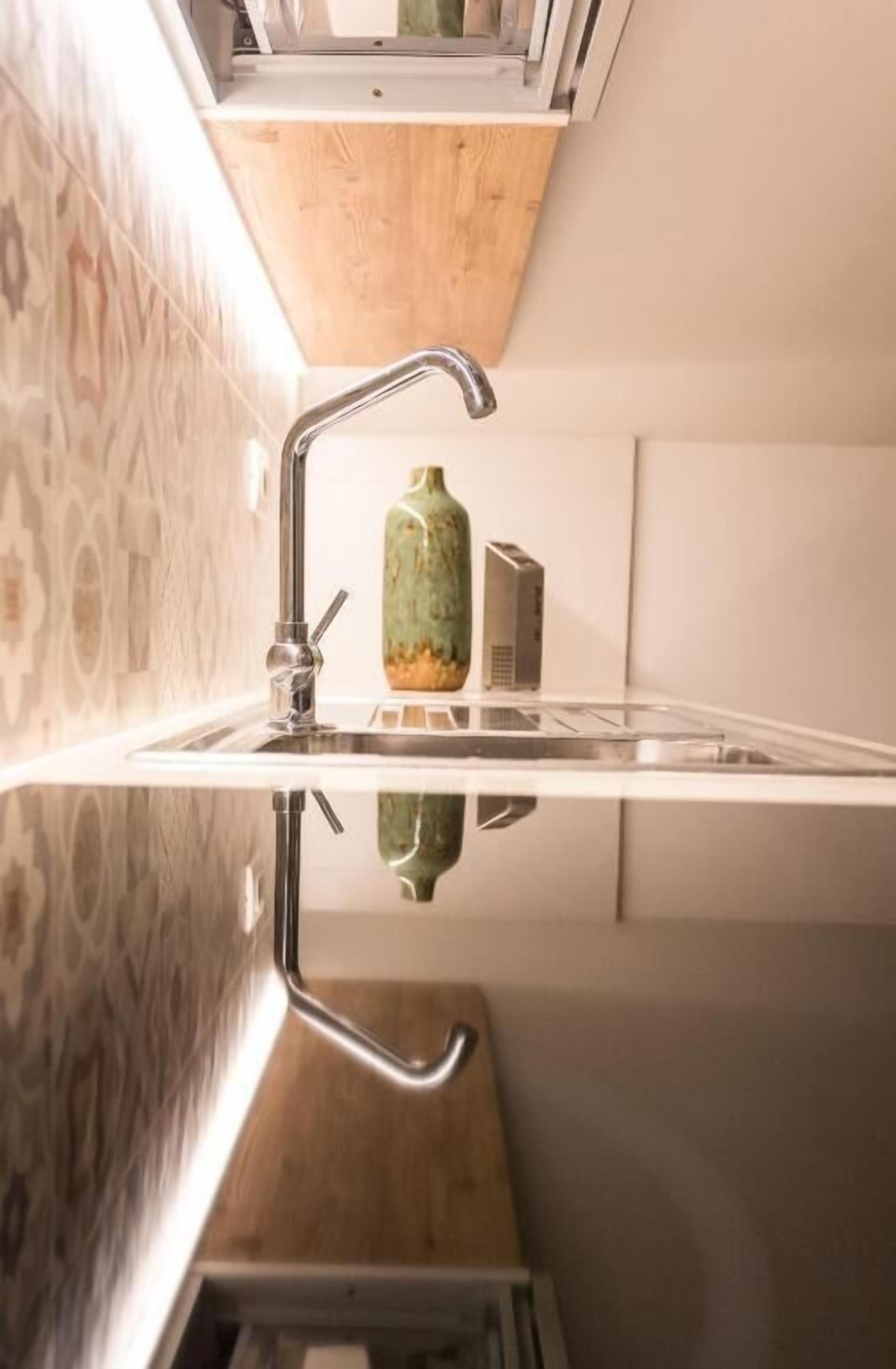 Una cocina con salpicadero reflectante, un grifo de acero inoxidable y un florero verde sobre la encimera.