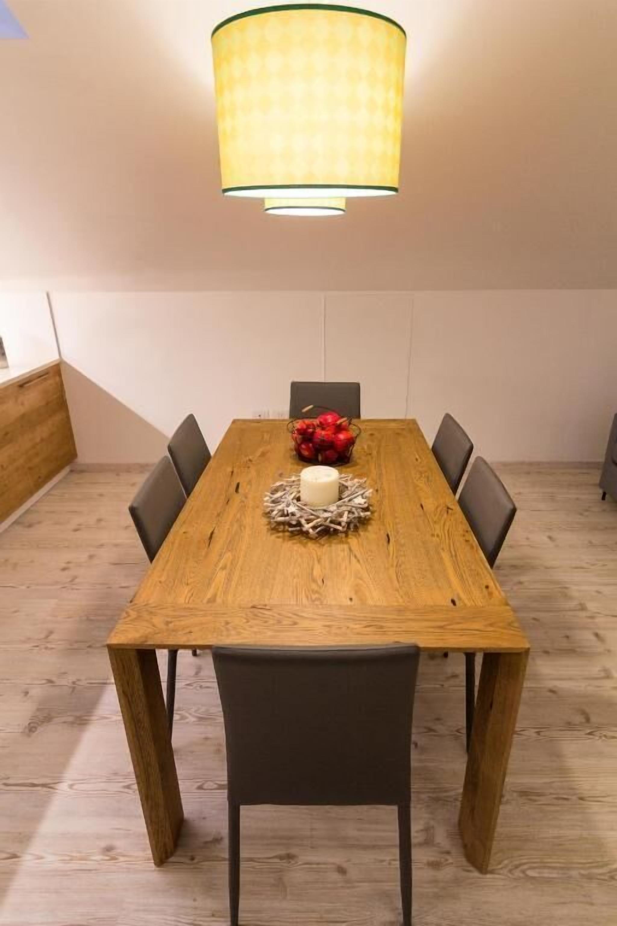 A dining area with a wooden table, six chairs, a central decorative item, and a hanging light fixture.