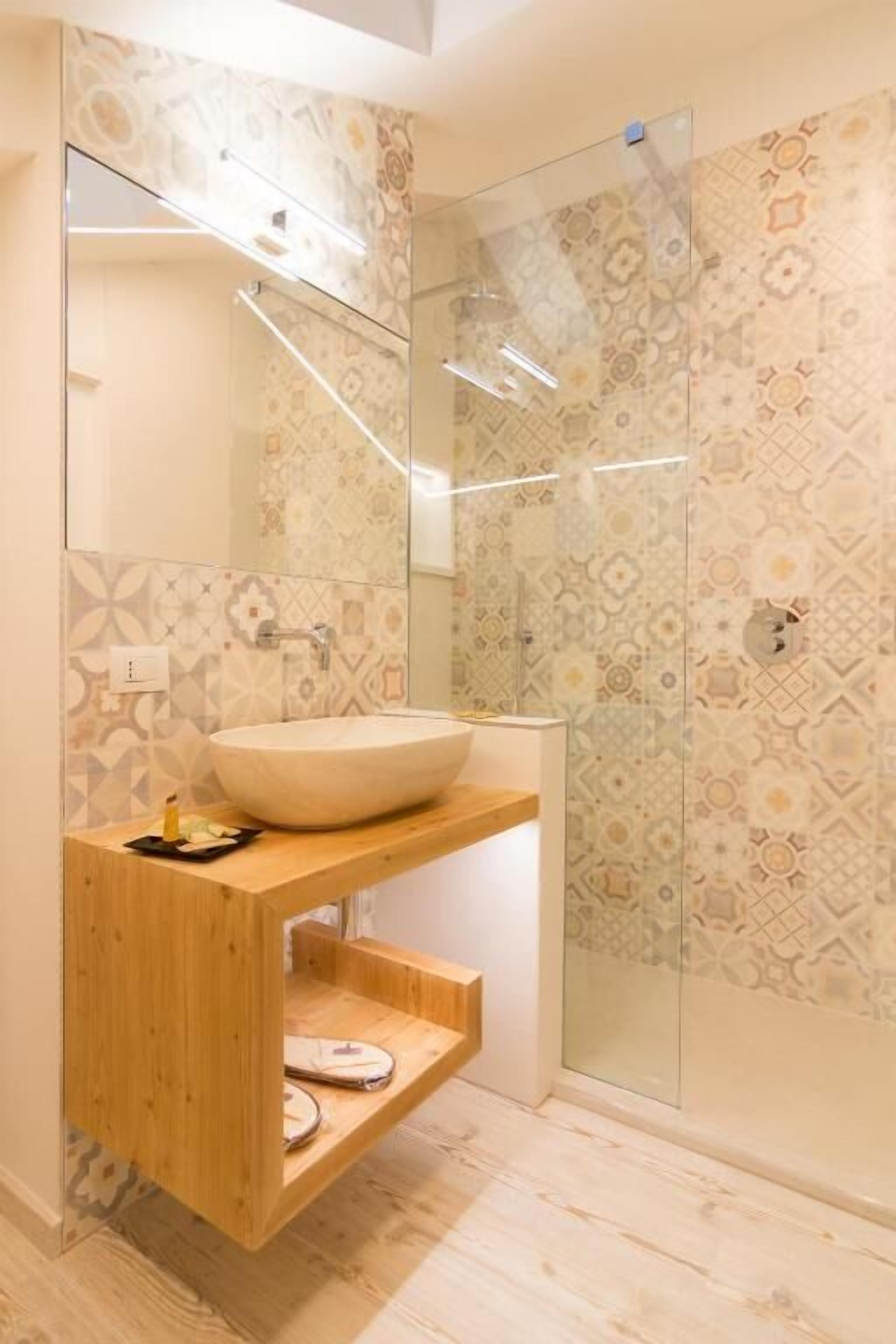 Un baño con un espejo grande, un lavabo sobre encimera, un mueble de tocador de madera y baldosas estampadas.