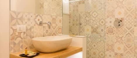 Un baño con un espejo grande, un lavabo sobre encimera, un mueble de tocador de madera y baldosas estampadas.
